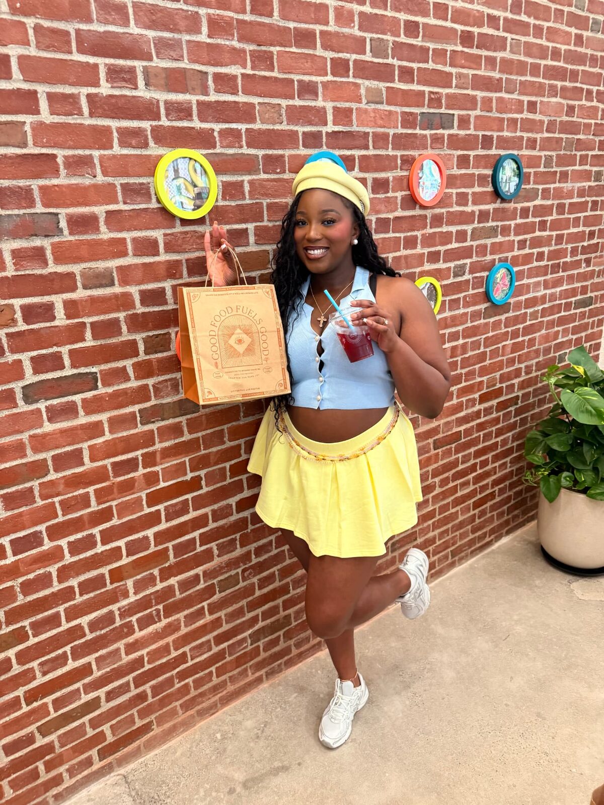 Fikayo with a Good Food Fuels Good bag and drink by a brick wall